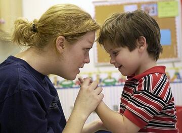 female teacher holding autistic boy's hands 