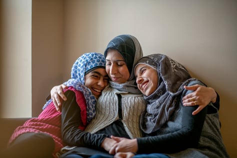 A refugee mother hugs both her daughters in her arms.