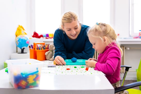 Toddler girl with autism in child occupational therapy session doing sensory playful exercises with her therapist.