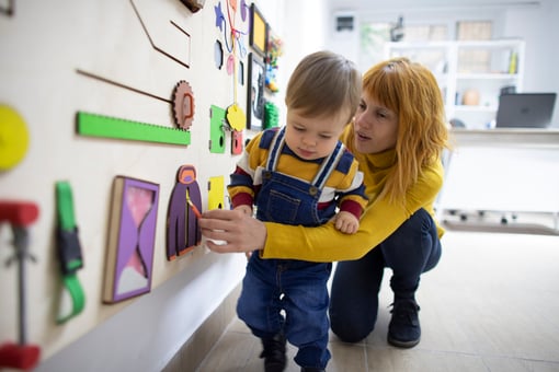 Young mother and her son with autism playing with wooden interactive board at psychotherapy office.