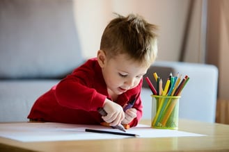 boy with autism writing with colored pencils on paper