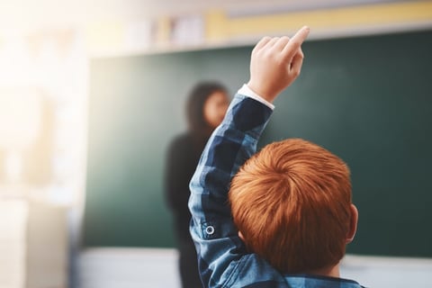 elementary school child with autism raising hand to ask questions in the class