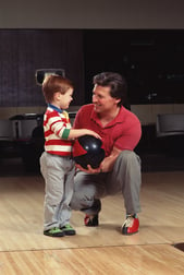 autistic boy holding bowling ball with father