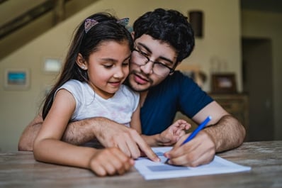 father sitting at a desk with daughter with autism in his lap and signing papers