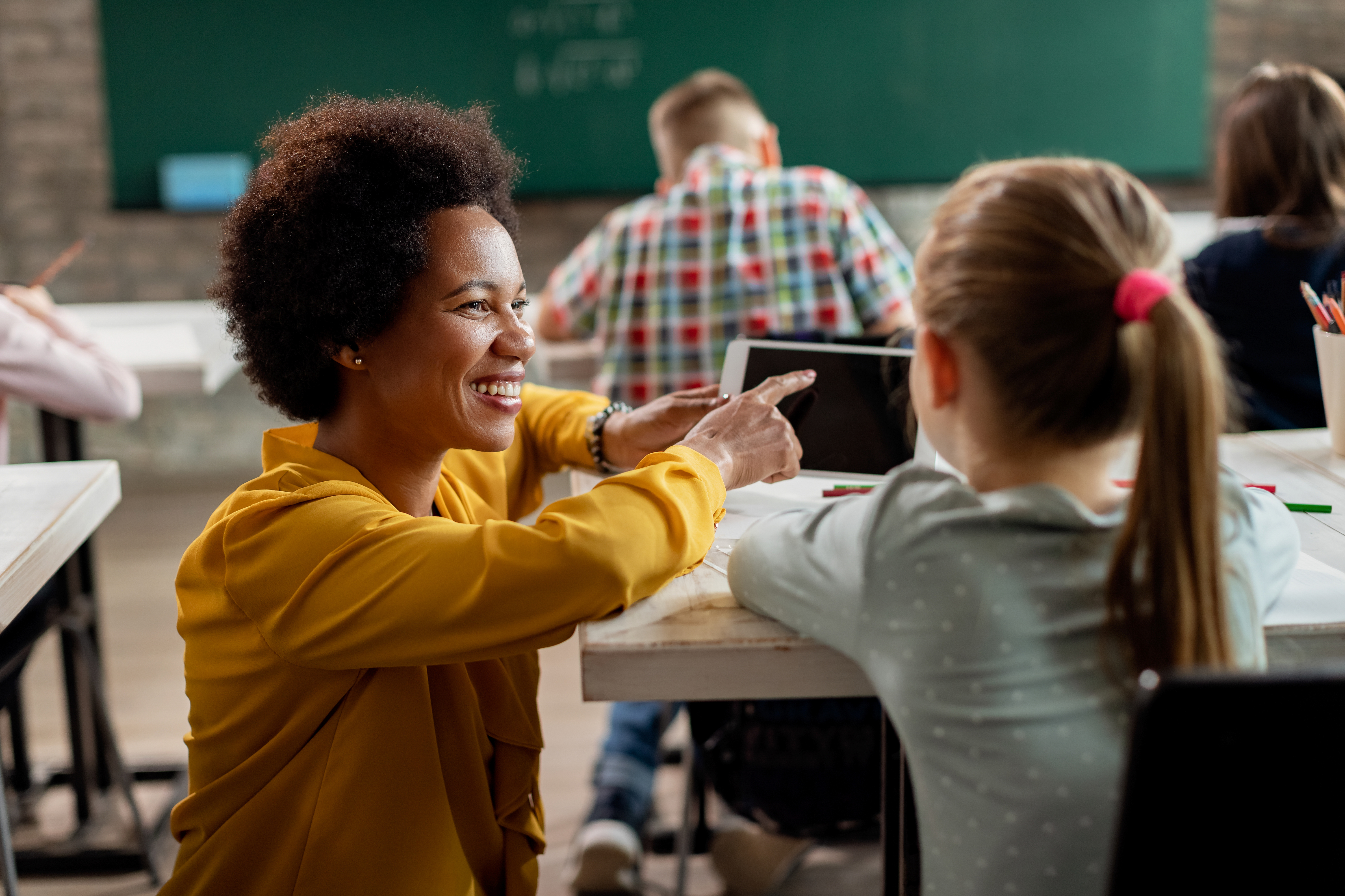 happy-black-teacher-schoolgirl-using-digital-tablet-classroom