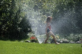 girl with autism running through sprinkler at summer camp