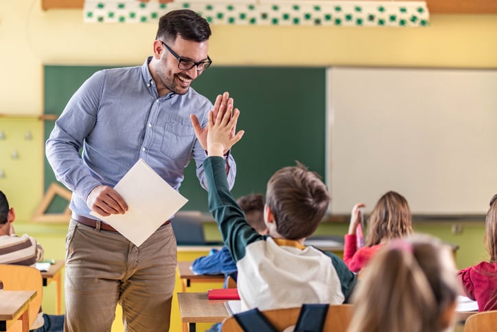 teacher giving high-five to his elementary student on a class in the classroom