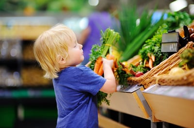 toddler boy with autism in a food store or a supermarket choosing fresh organic carrots